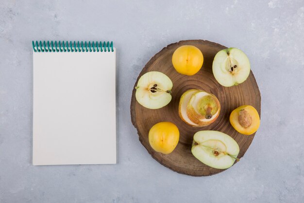 Manzana, pera y duraznos en un trozo de madera, con un cuaderno a un lado