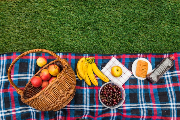 Manzana; plátano; guindas; Servilleta y hojaldre con botella de agua sobre una manta sobre hierba verde