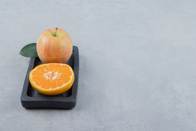 Manzana y rodaja de naranja sobre placa negra