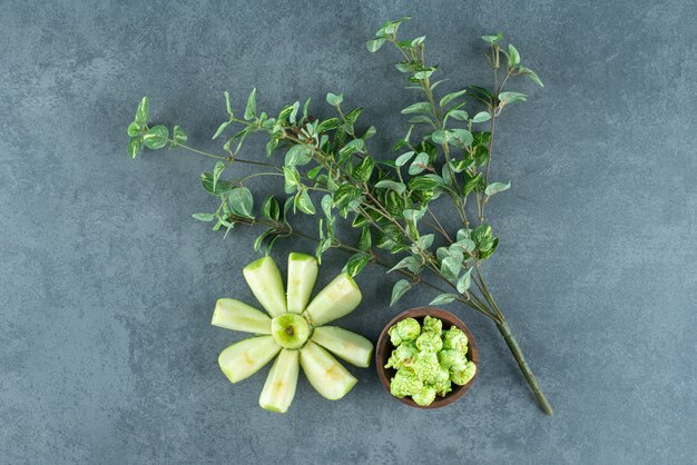 Manzana en rodajas prolijas dispuesta con una planta decorativa y un tazón pequeño de dulces de palomitas de maíz sobre fondo de mármol. Foto de alta calidad