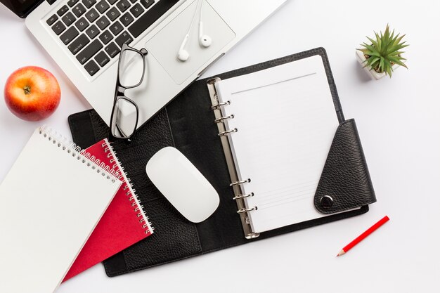 Manzana roja, agenda, mouse, lentes, audífonos, lápiz y computadora portátil en el escritorio blanco