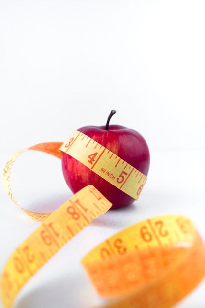 Foto gratuita manzana roja con cinta métrica en mesa blanca