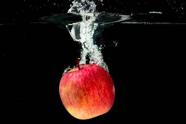 Manzana roja entera cayendo en agua sobre fondo negro