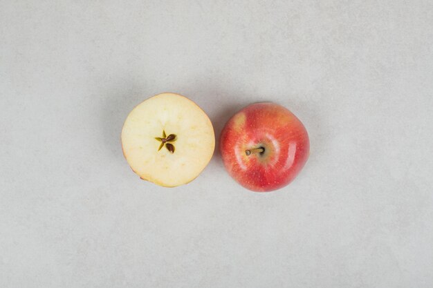 Manzana roja entera y medio cortada sobre superficie gris.