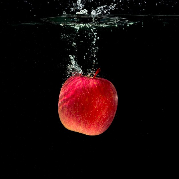 Manzana roja entera que salpica en agua contra fondo negro