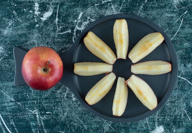 Foto gratuita manzana roja entera y en rodajas sobre plancha de madera oscura.