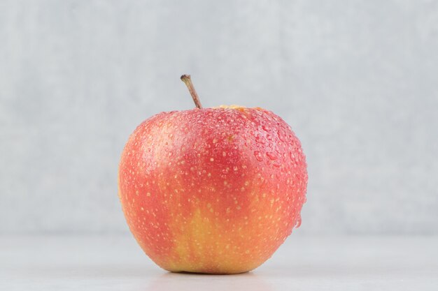 Manzana roja con gotas de agua sobre la mesa de piedra.