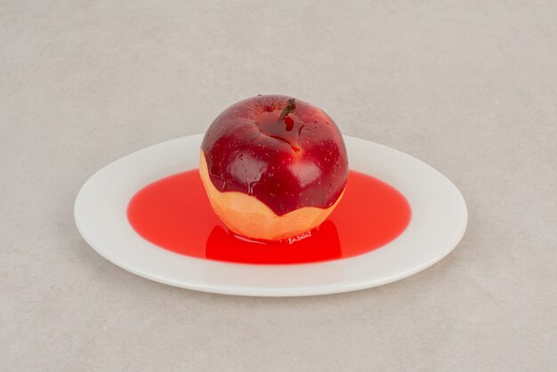 Manzana roja pelada en jugo en plato blanco.