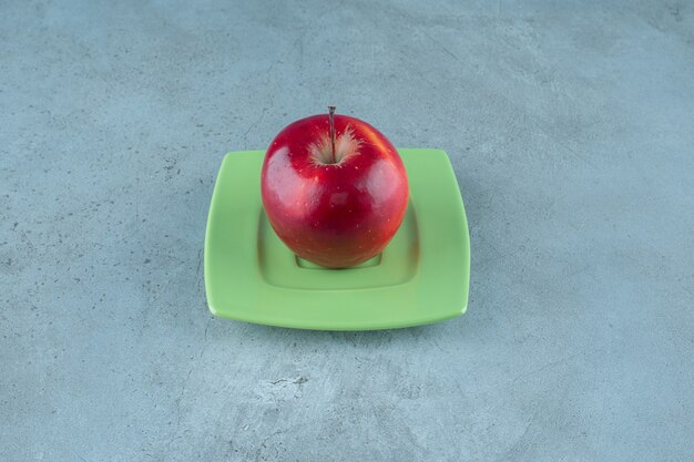 Manzana roja en un plato, sobre el fondo de mármol. Foto de alta calidad