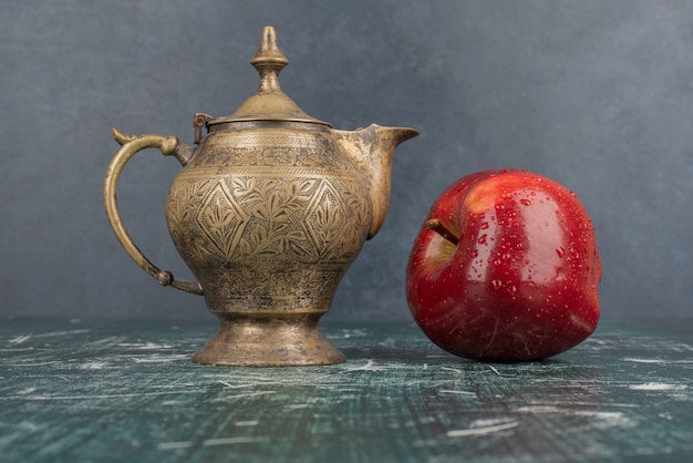 Manzana roja y tetera clásica sobre mesa de mármol.