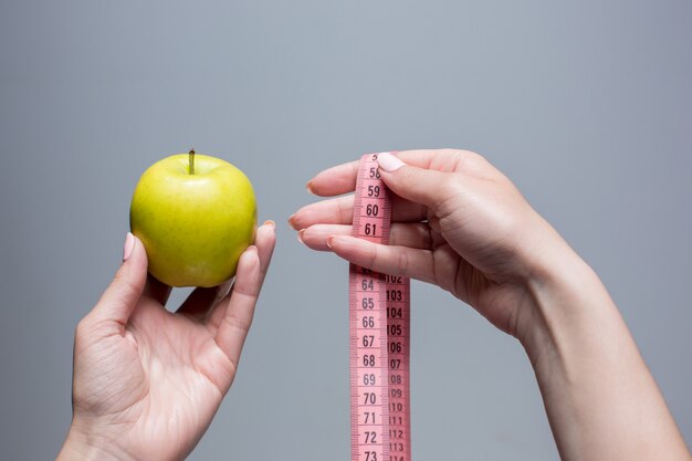 Manzana verde y cinta métrica en manos femeninas en pared gris