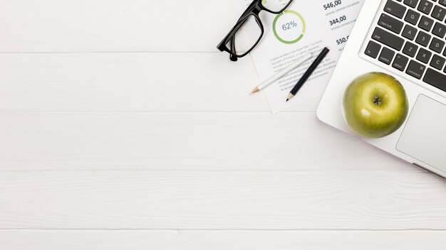 Manzana verde en la computadora portátil con lápices de colores y lentes en el plan de presupuesto sobre el escritorio