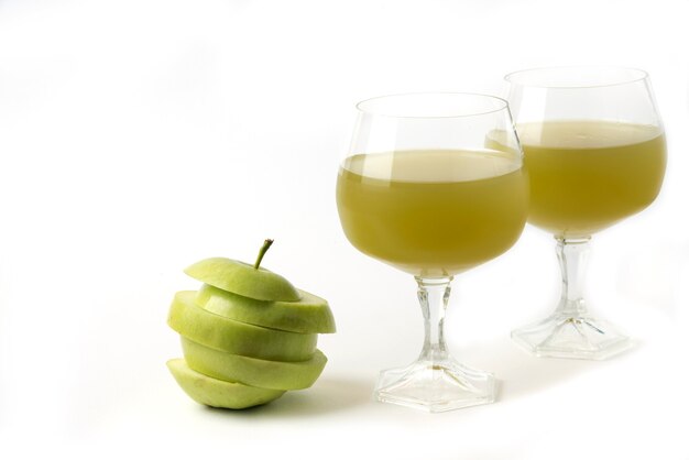 Manzana verde entera y en rodajas en blanco con un vaso de jugo