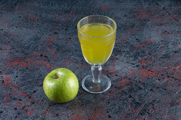 Una manzana verde entera con un vaso de jugo colocado sobre la mesa de piedra.