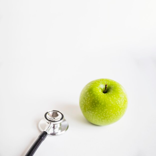 Manzana verde fresca y un estetoscopio sobre fondo blanco