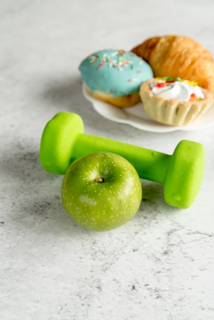 Manzana verde y mancuerna con alimentos dulces sobre fondo de hormigón