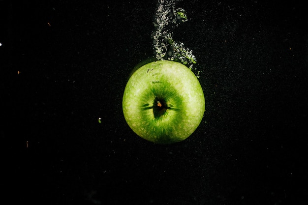 Manzana verde salpica el agua que cae sobre fondo negro