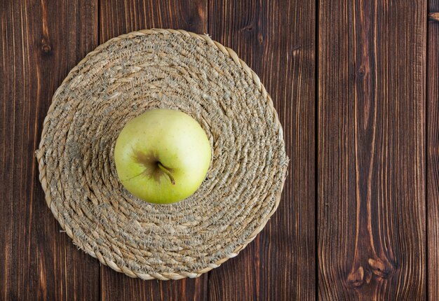 Manzana verde sobre un salvamanteles y fondo de madera. vista superior.