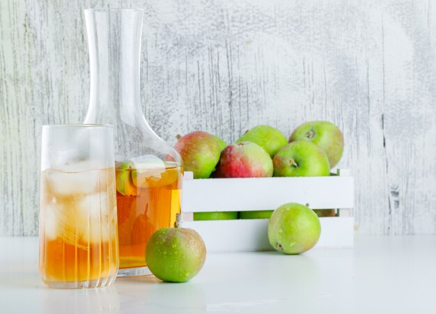 Manzanas con bebidas en una caja de madera en blanco y sucio, vista lateral.