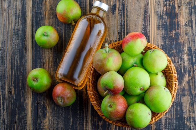 Manzanas con botella de bebida en una canasta sobre fondo de madera, plano laical.