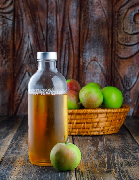 Foto gratuita manzanas con botella de bebida en una canasta sobre fondo de madera, vista lateral.