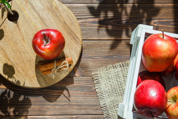 Manzanas en una caja blanca y manzana con palitos de canela en la tabla de cortar
