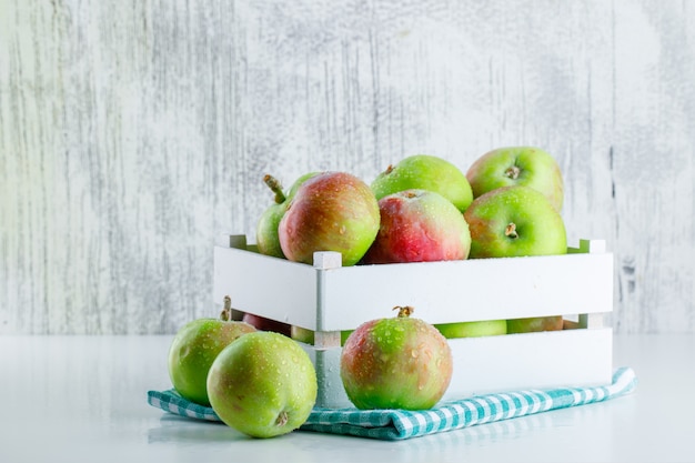 Manzanas en una caja de madera con vista lateral de tela de picnic en blanco y sucio