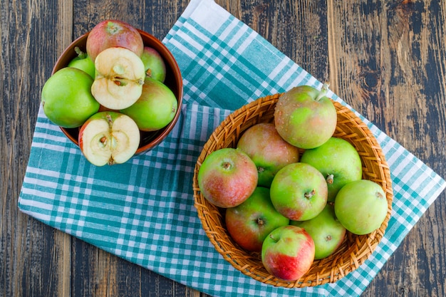 Manzanas en canasta de mimbre y cuenco sobre fondo de tela de madera y picnic. vista superior.