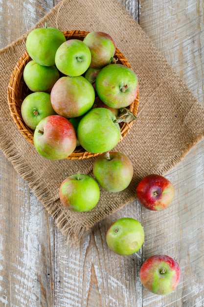 Manzanas en una canasta de mimbre sobre madera y pedazo de saco. vista superior.