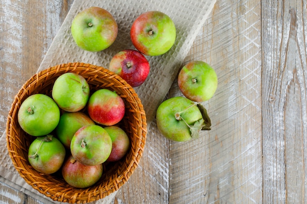 Manzanas en una canasta de mimbre sobre madera y toalla de cocina.