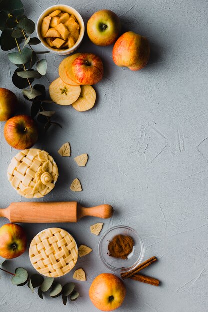 Manzanas y canela cerca de pasteles y rodillo