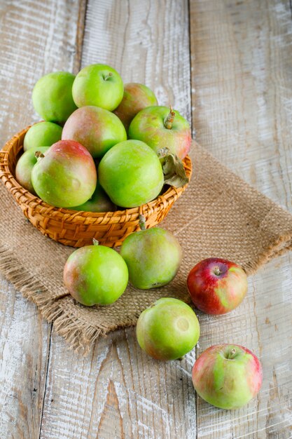 Manzanas en una cesta de mimbre vista de ángulo alto en madera y pedazo de saco