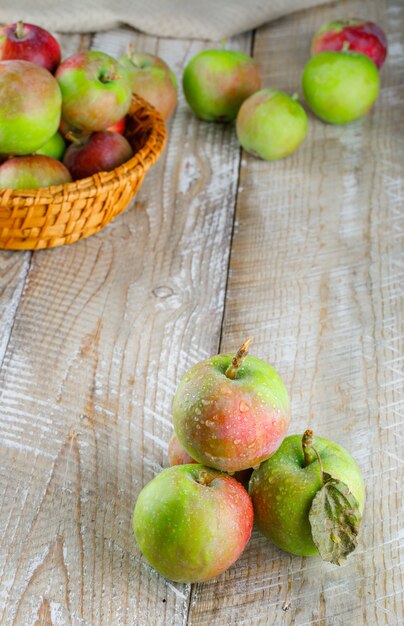 Las manzanas en una cesta de mimbre vista de ángulo alto en madera y toalla de cocina