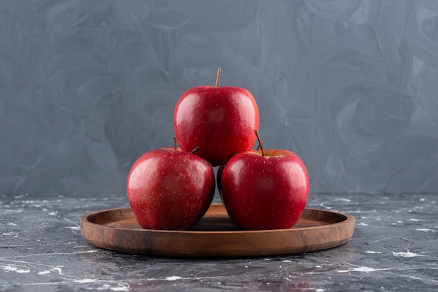 Manzanas enteras rojas brillantes colocadas sobre placa de madera.