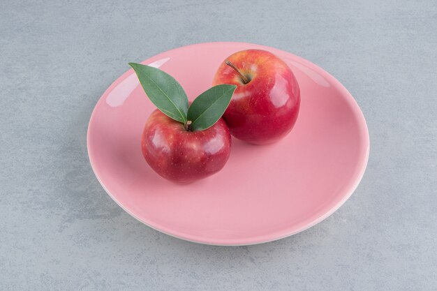 Manzanas frescas en un plato rosa sobre mármol.