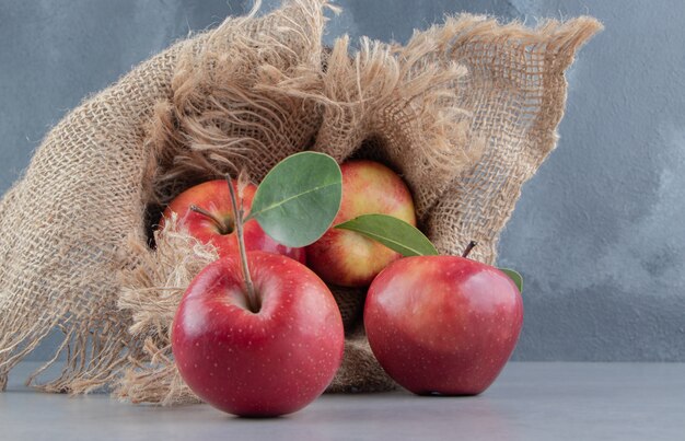 Manzanas frescas saliendo de una canasta cubierta de tela en mármol.