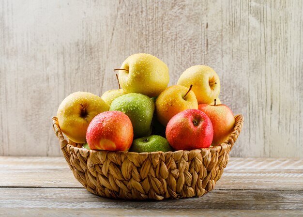 Manzanas con gotas en una cesta de mimbre en madera clara y grunge