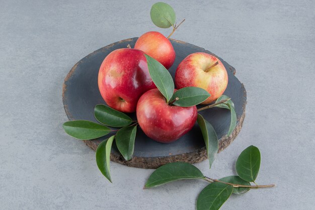 Manzanas y hojas agrupadas sobre una tabla de madera sobre mármol.