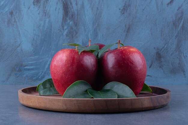 Manzanas y hojas en el tablero sobre la superficie oscura.