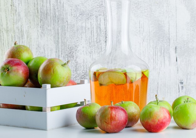Manzanas con jugo en una caja de madera en blanco y sucio, vista lateral.