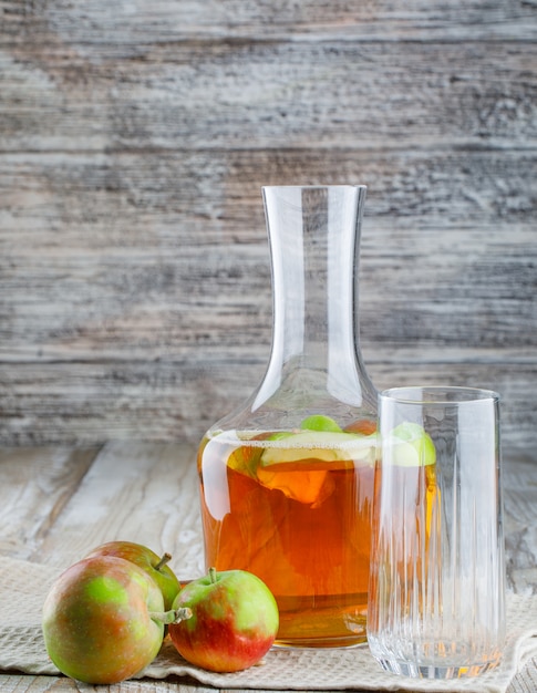 Manzanas con jugo, vidrio sobre madera y toalla de cocina, vista lateral.