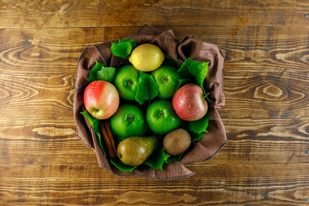 Manzanas con limón, pera, kiwi, canela, hojas en la mesa de madera