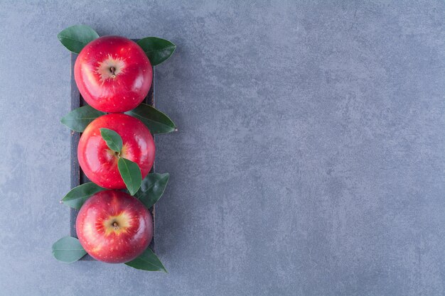 Manzanas maduras y frescas con hojas en bandeja de madera sobre la superficie oscura