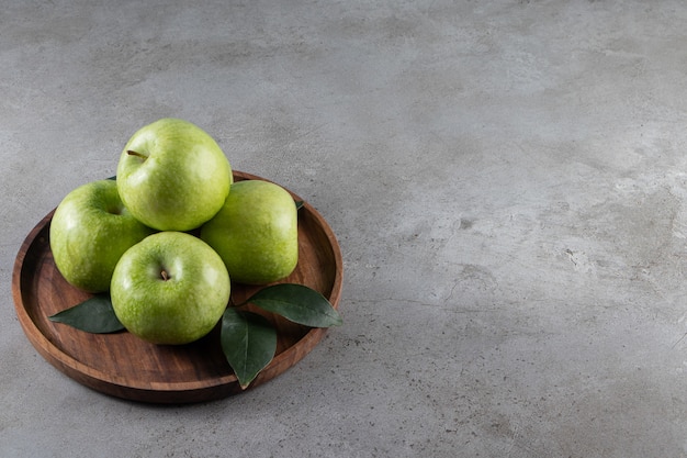 Manzanas maduras en una placa de madera, sobre la mesa de mármol.