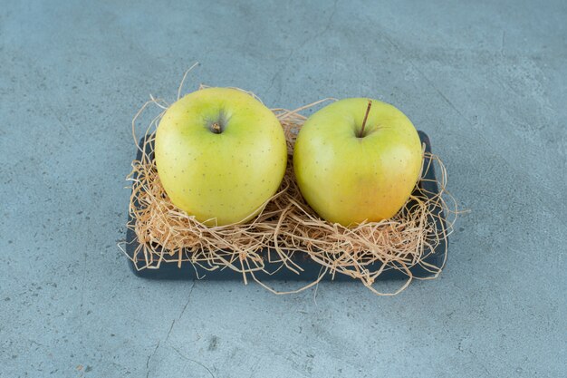 Manzanas maduras sobre paja seca y sobre una tabla, sobre el fondo de mármol. Foto de alta calidad