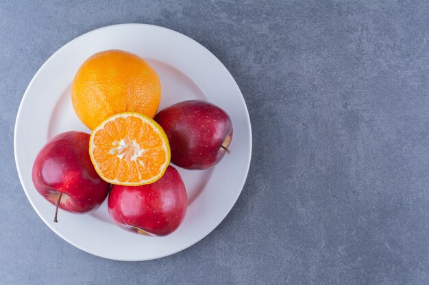 Manzanas y naranja en placa sobre mesa de mármol.