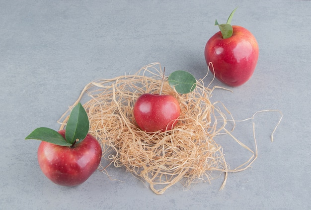 Manzanas y un pequeño montón de paja sobre mármol.