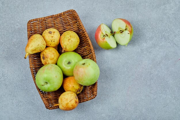 Manzanas y peras en la canasta en gris.