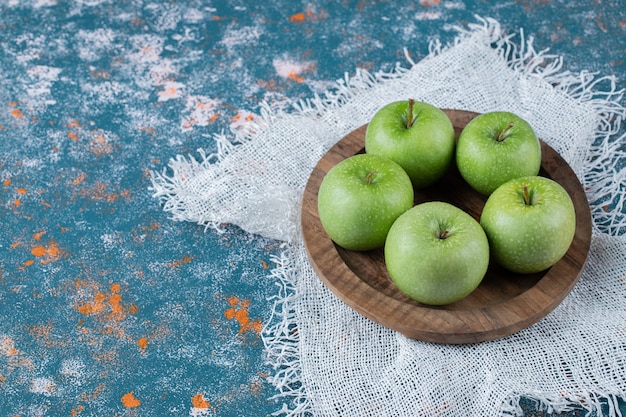 Foto gratuita manzanas en una placa de madera sobre una mesa de textura azul.