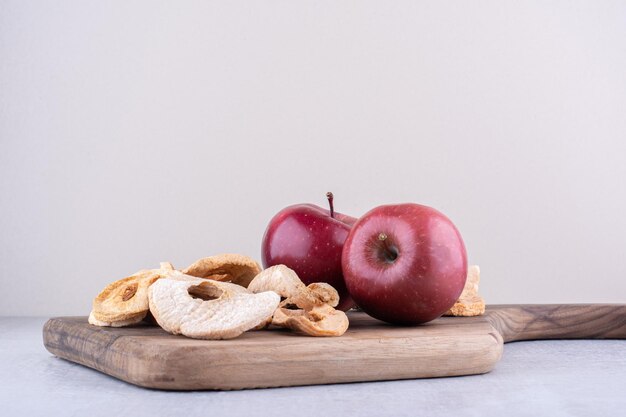 Manzanas y rodajas de manzana seca en una placa sobre superficie blanca